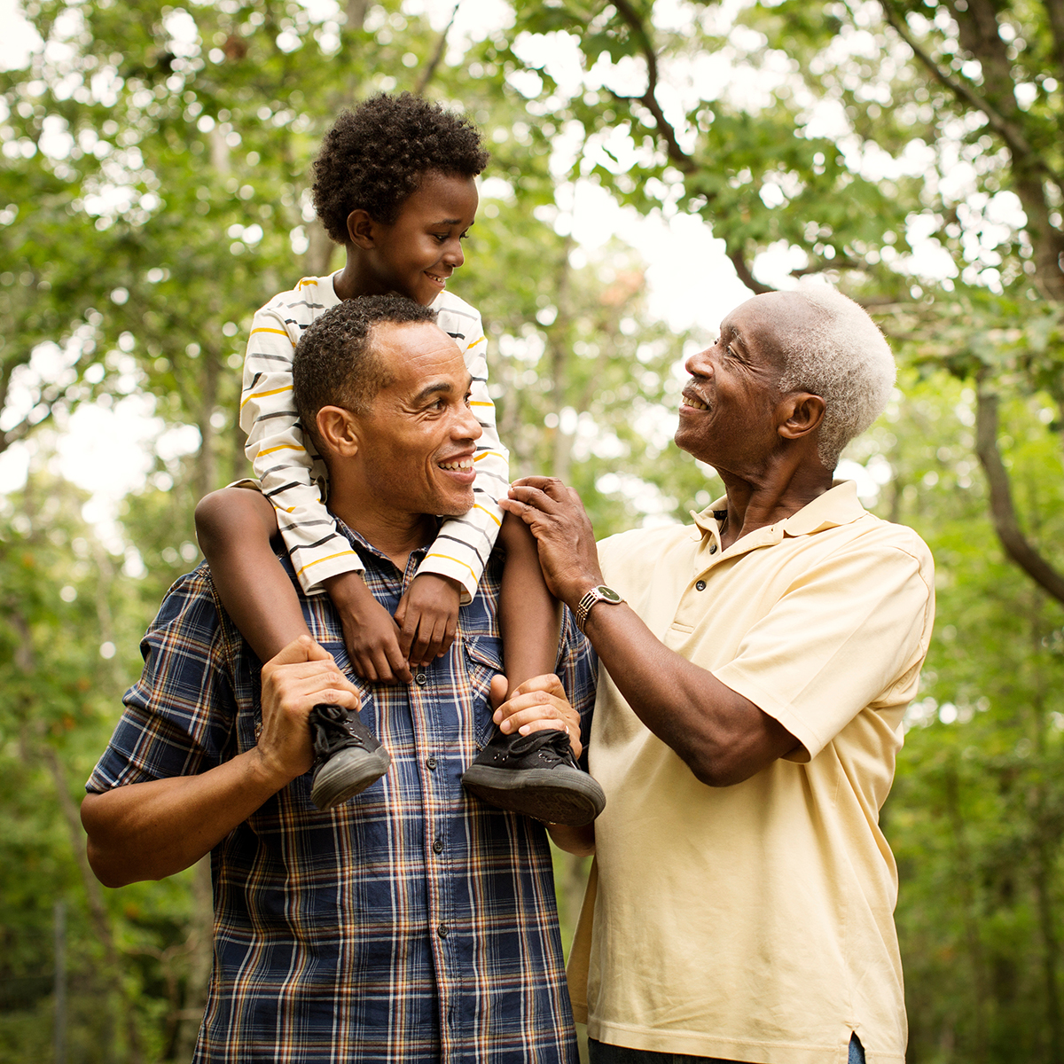 Three generations of black men. A boy being carried on his fathers shoulders, and his grandfather