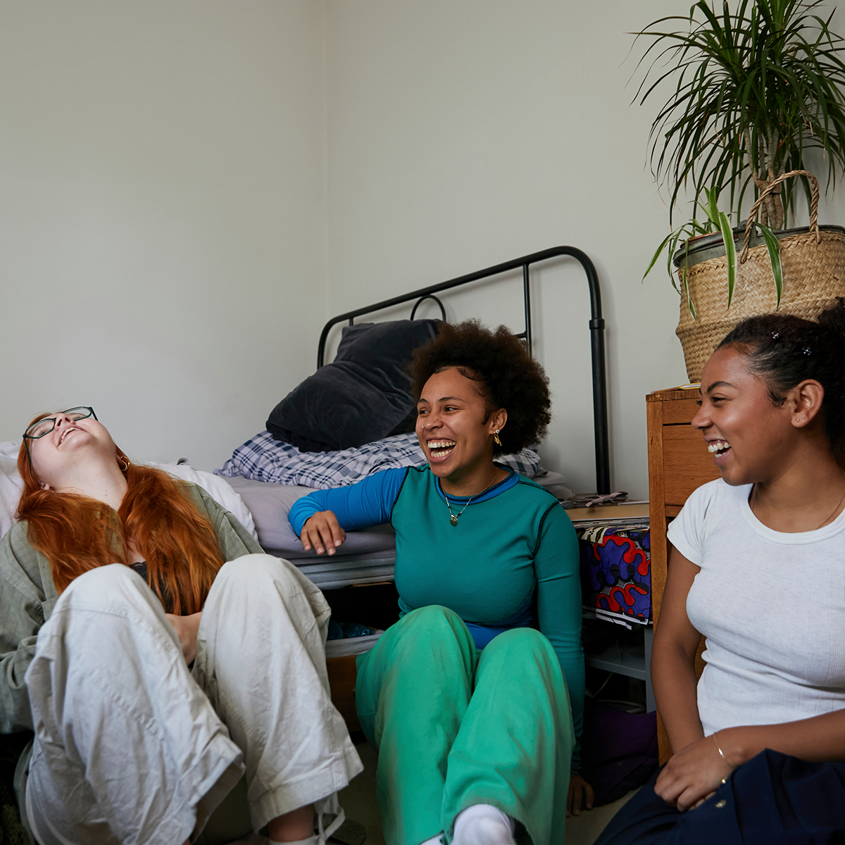 three women living together laughing in bedroom Three women sitting on the floor of a bedroom laughing together living in community